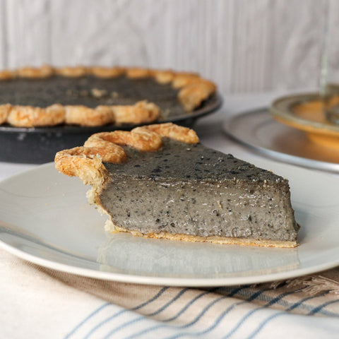 Slice of black sesame pie on a plate with the rest of the pie in the background.