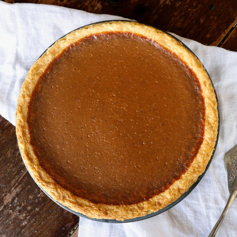 Pumpkin pie on a wooden table with a white cloth and pie server.